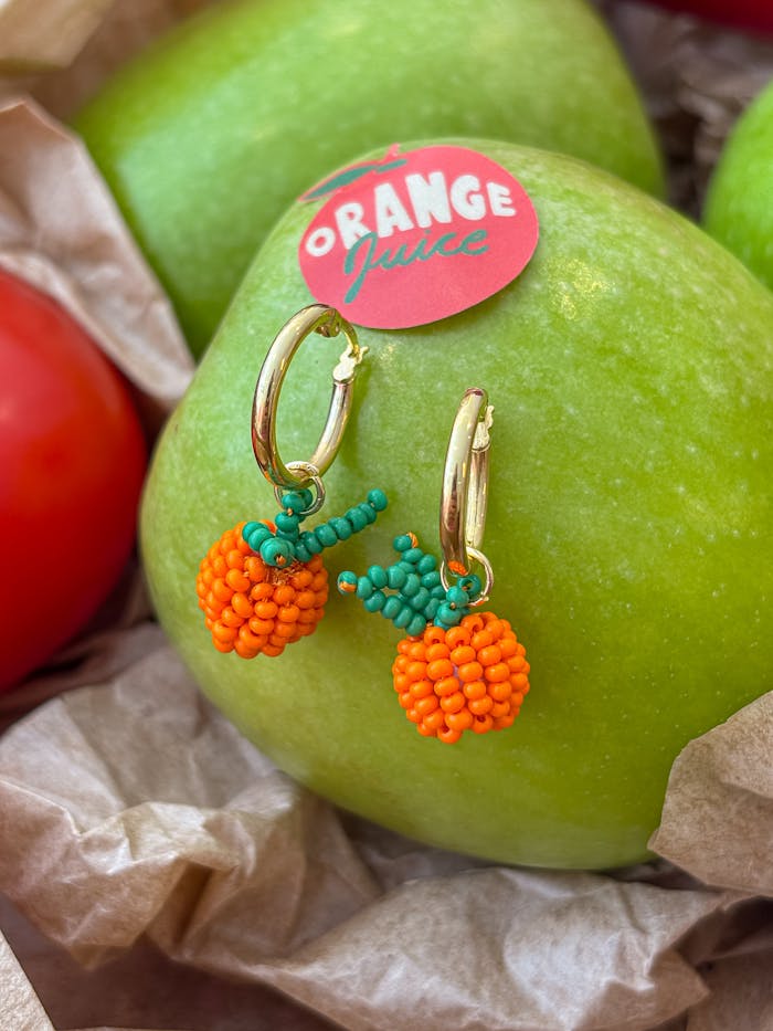 about-us Vibrant handmade beaded earrings styled on a crisp green apple backdrop.